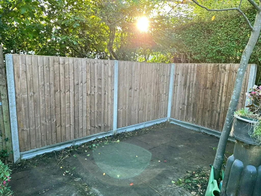 Closeboard fence panels with concrete posts installed in a shaded corner garden area.
