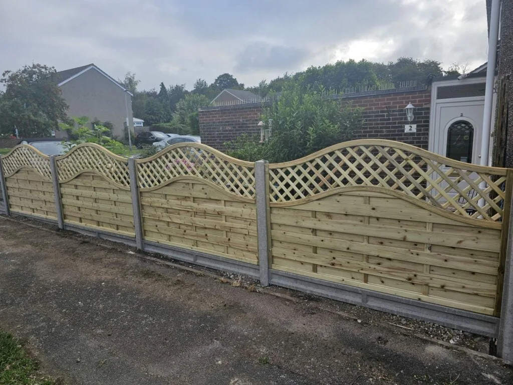 Decorative omega lattice fence panels with arched tops installed along a driveway, supported by concrete posts.