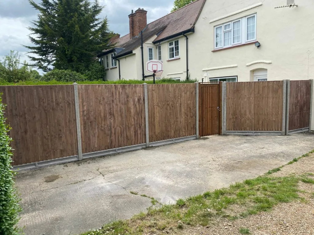 Wooden fence panels installed with concrete posts and a wooden gate, enclosing a residential driveway in front of a cream-colored house.